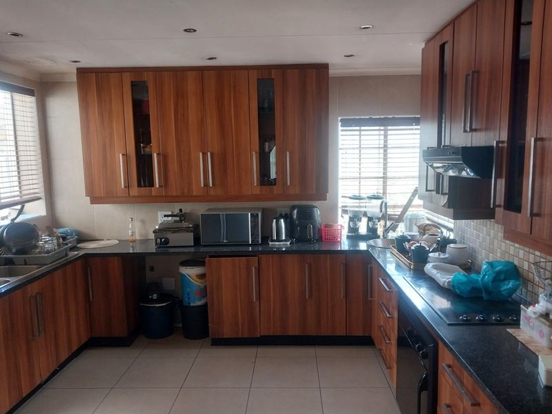 A functional kitchen featuring wood-grain cabinetry, dark granite countertops, tiled flooring, and integrated appliances including a hob and extractor fan.