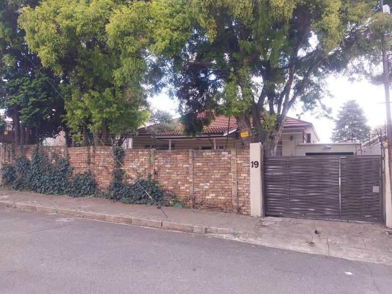 Street view of a residential property featuring a brick boundary wall, metal sliding gate, and mature trees providing privacy to the front facade.