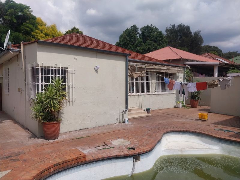 Rear exterior view of the house featuring a swimming pool, brick paved patio area, and security bars on windows.