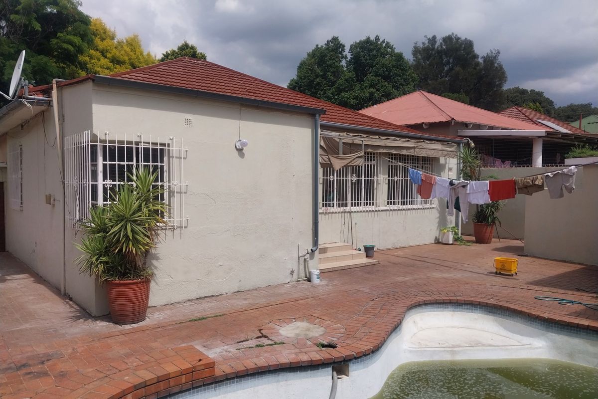 Rear exterior view of the house featuring a swimming pool, brick paved patio area, and security bars on windows.