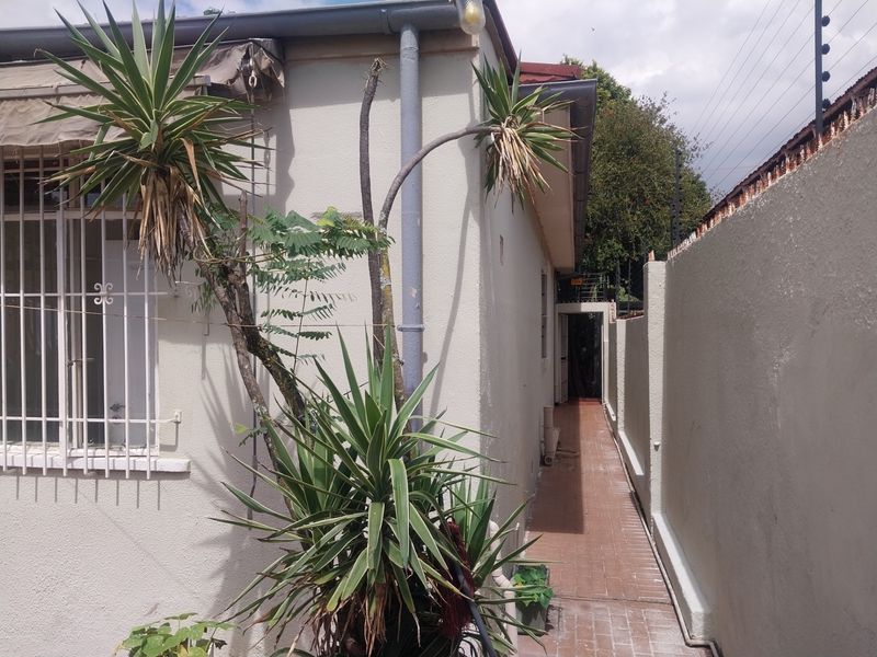 A narrow side passage of the house featuring paved flooring, security bars on windows, and an exterior wall with integrated drainage pipes.
