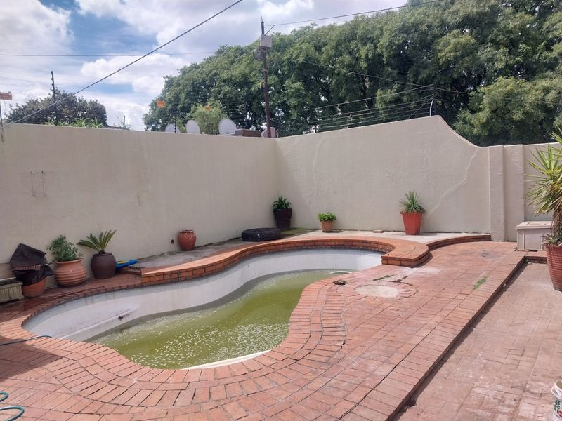 Outdoor pool area featuring a kidney-shaped swimming pool with brick coping and surrounding paved patio, enclosed by a high boundary wall.