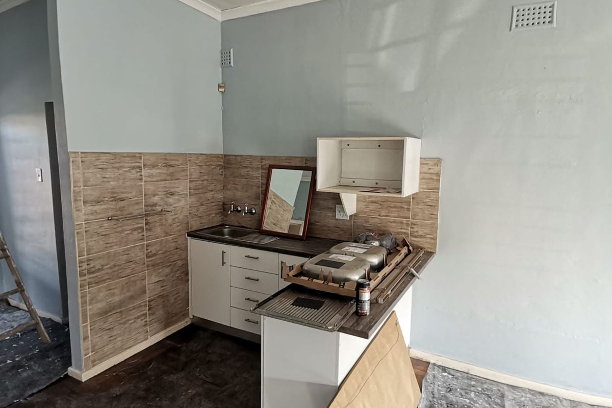 A compact kitchenette area featuring tiled splashbacks, a stainless steel sink, and built-in cabinetry, currently undergoing maintenance or renovation.