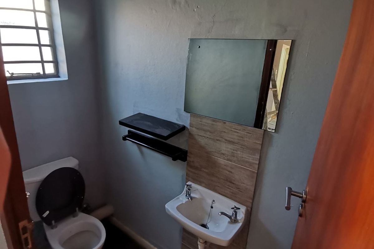 A compact office restroom featuring a wall-mounted basin with tiled splashback, a mirror, and a standard toilet.