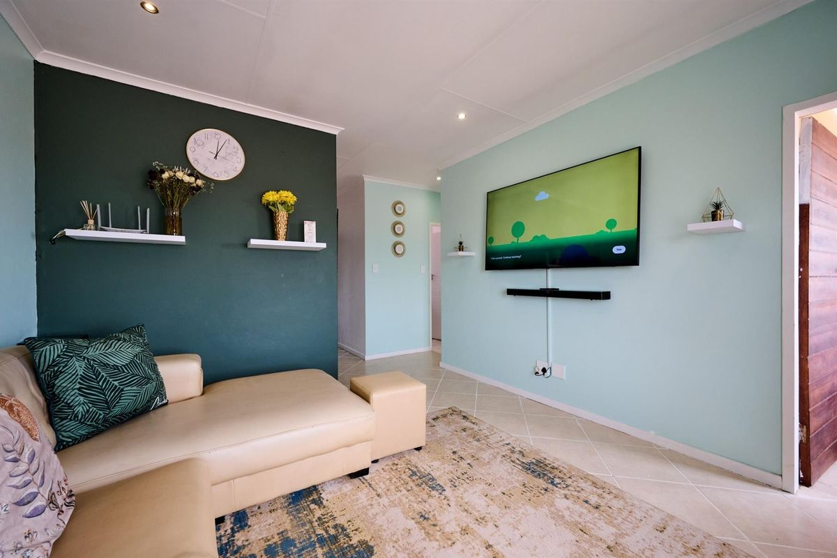 A well-maintained living room featuring a contrasting dark green accent wall, light blue walls, and tiled flooring.