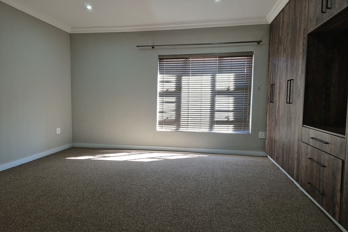 A spacious bedroom featuring neutral carpeting, recessed ceiling lighting, and extensive built-in wooden cabinetry with integrated storage.