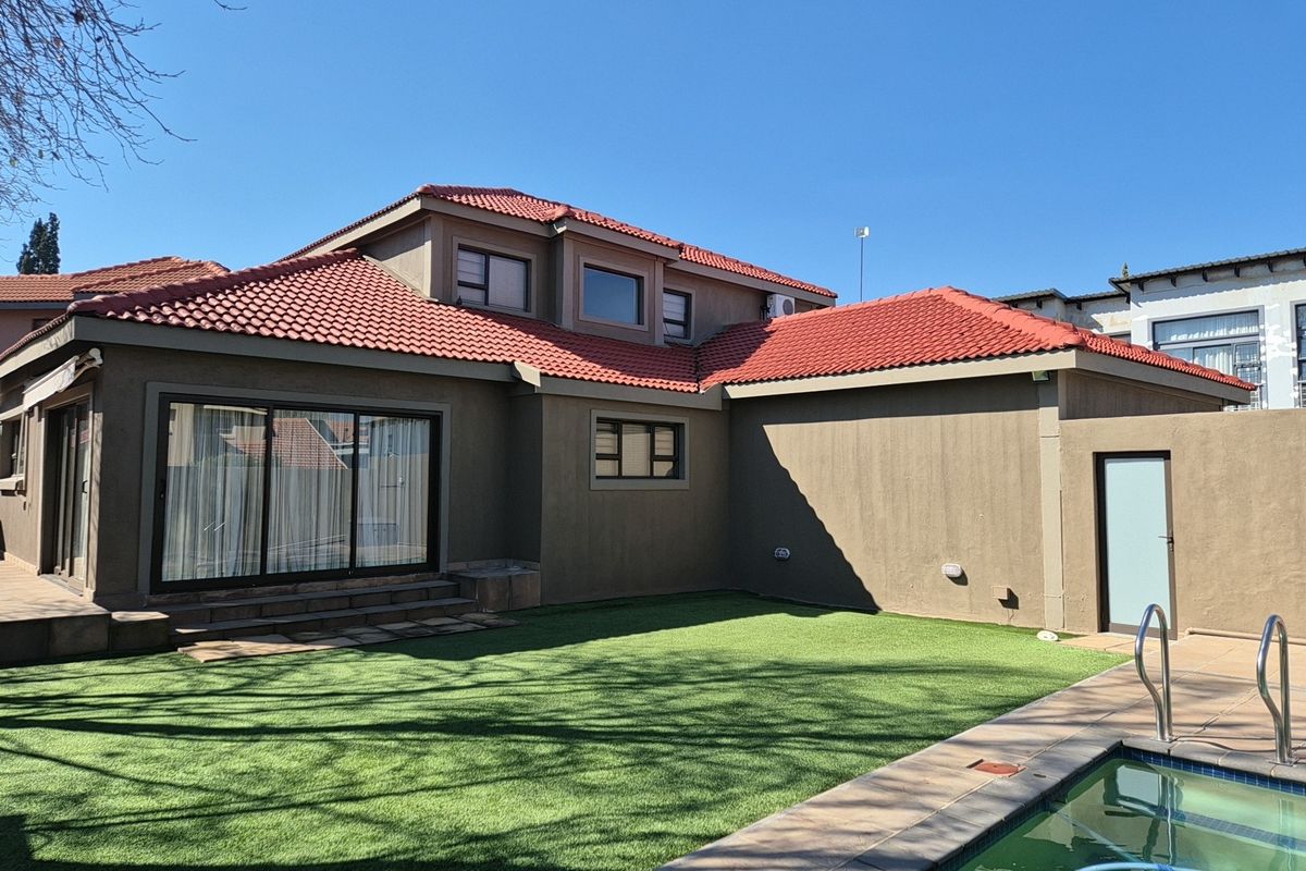 Rear view of the house featuring a tiled roof, sliding glass doors, a well-maintained artificial lawn, and a swimming pool.