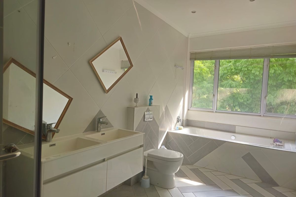 Modern bathroom featuring a double vanity, wall-mounted toilet, and a built-in bathtub with large windows providing natural light and garden views.