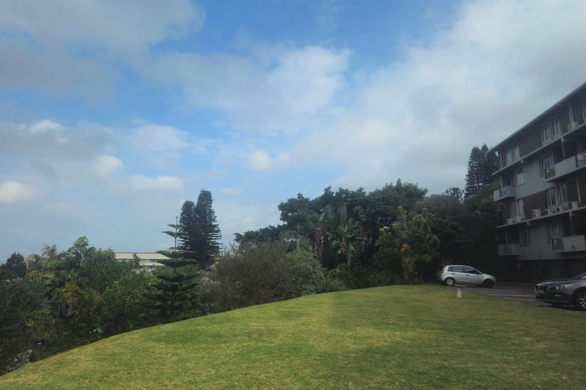 A view of the apartment complex exterior featuring a well-maintained lawn area and surrounding mature trees.