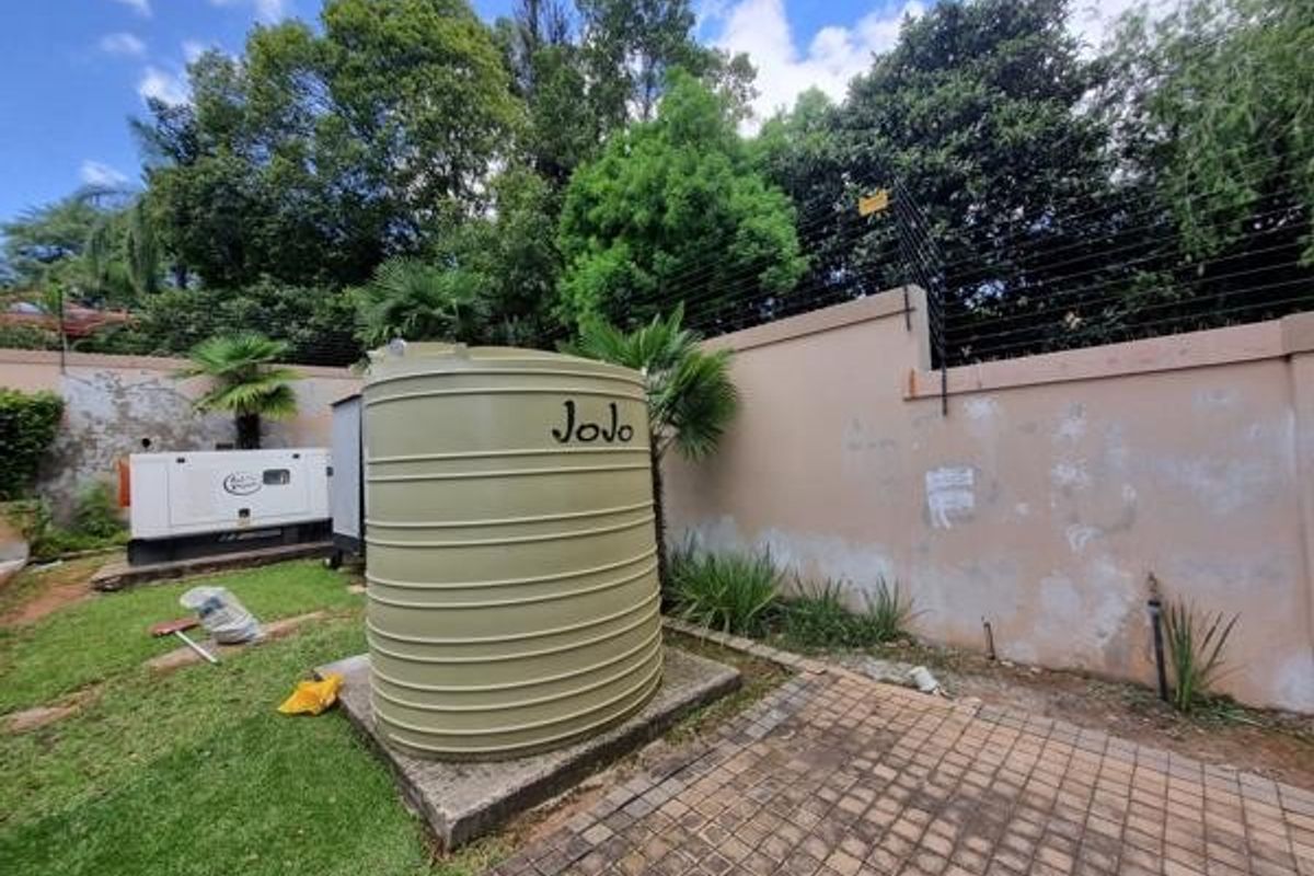 Rear garden area featuring a water storage tank, backup generator, and perimeter wall with electric fencing.