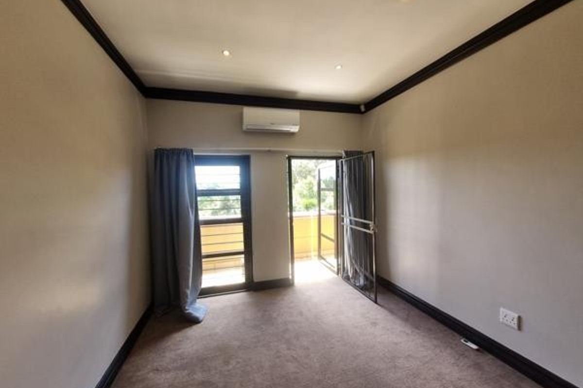 Spacious bedroom featuring neutral walls, dark trim, carpeted flooring, an integrated air conditioning unit, and direct access to an outdoor balcony area.