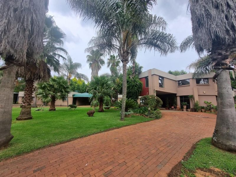 A well-maintained farm property featuring a brick-paved driveway leading to a multi-level residence surrounded by mature palm trees and a lush green garden.