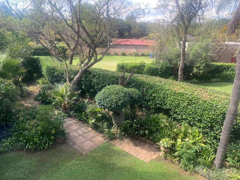 A well-maintained garden featuring a paved walkway, lush green lawn, mature trees, and established hedging, providing a private and serene outdoor space.