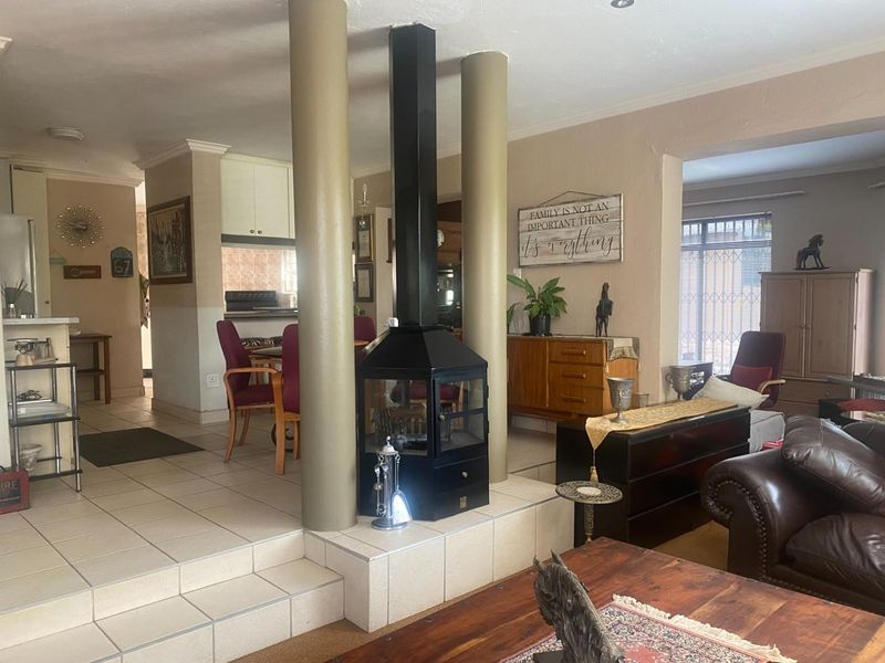 Open plan living and dining area featuring a central freestanding fireplace, tiled flooring, and structural columns connecting to the kitchen space.