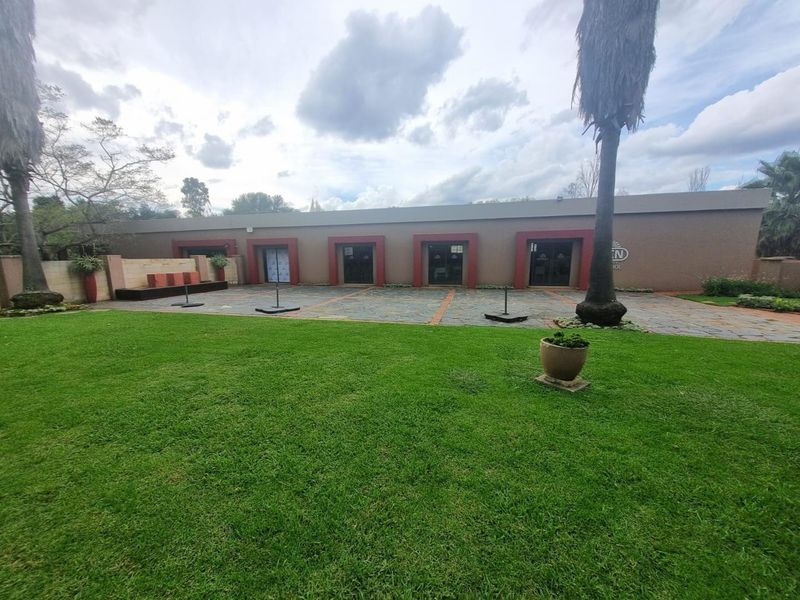 A spacious rear exterior view featuring a large manicured lawn, stone-paved patio area, and multiple glass sliding door access points to the main building.