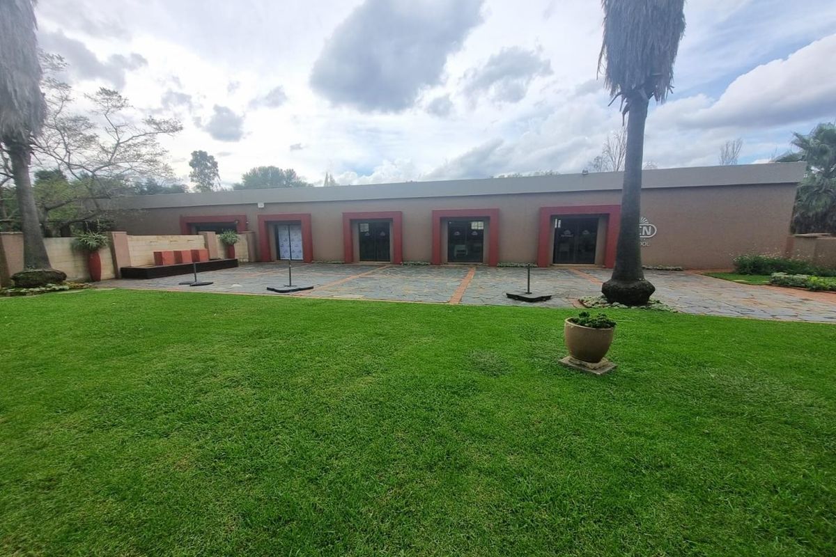 A spacious rear exterior view featuring a large manicured lawn, stone-paved patio area, and multiple glass sliding door access points to the main building.