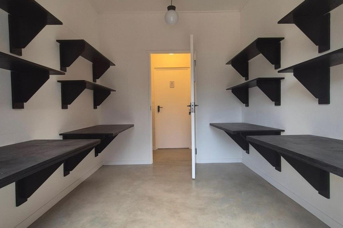 A functional office or utility space featuring built-in wall shelving and desk surfaces, finished with polished concrete flooring and modern pendant lighting.