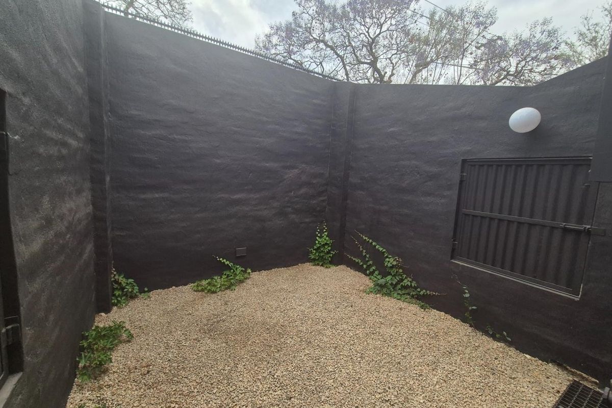 A private, enclosed courtyard area featuring dark painted perimeter walls, gravel ground cover, and integrated wall-mounted lighting.