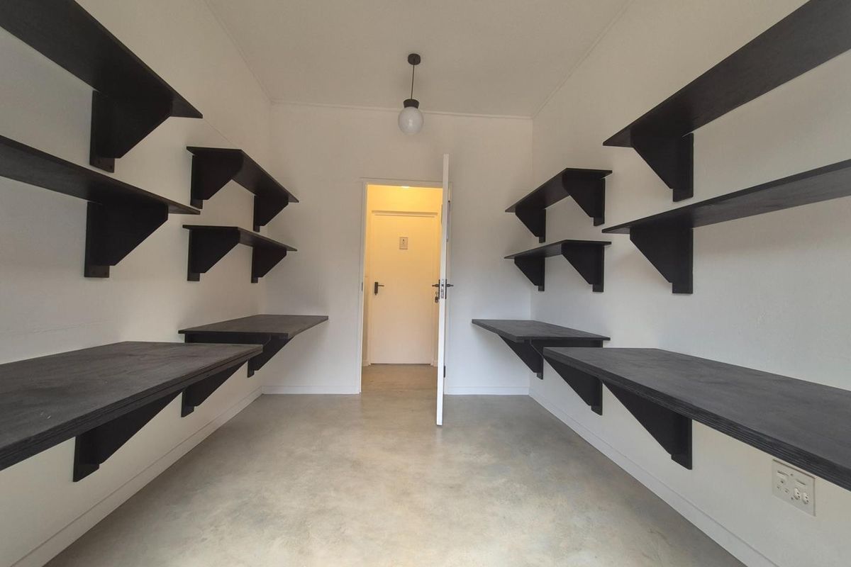 A functional office space featuring built-in dark timber shelving and desk surfaces, polished concrete flooring, and a central pendant light fixture.