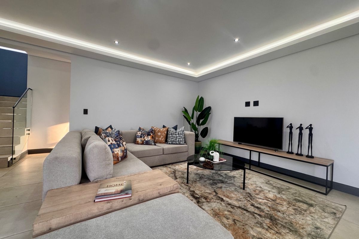 Modern living room featuring recessed tray ceiling lighting, tiled flooring, and a staircase with glass balustrades in the background.