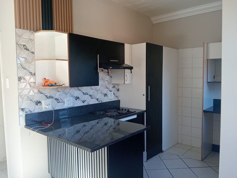 A compact kitchen featuring modern black and white cabinetry, granite countertops, a built-in hob with extractor fan, and decorative geometric tiled backsplash.