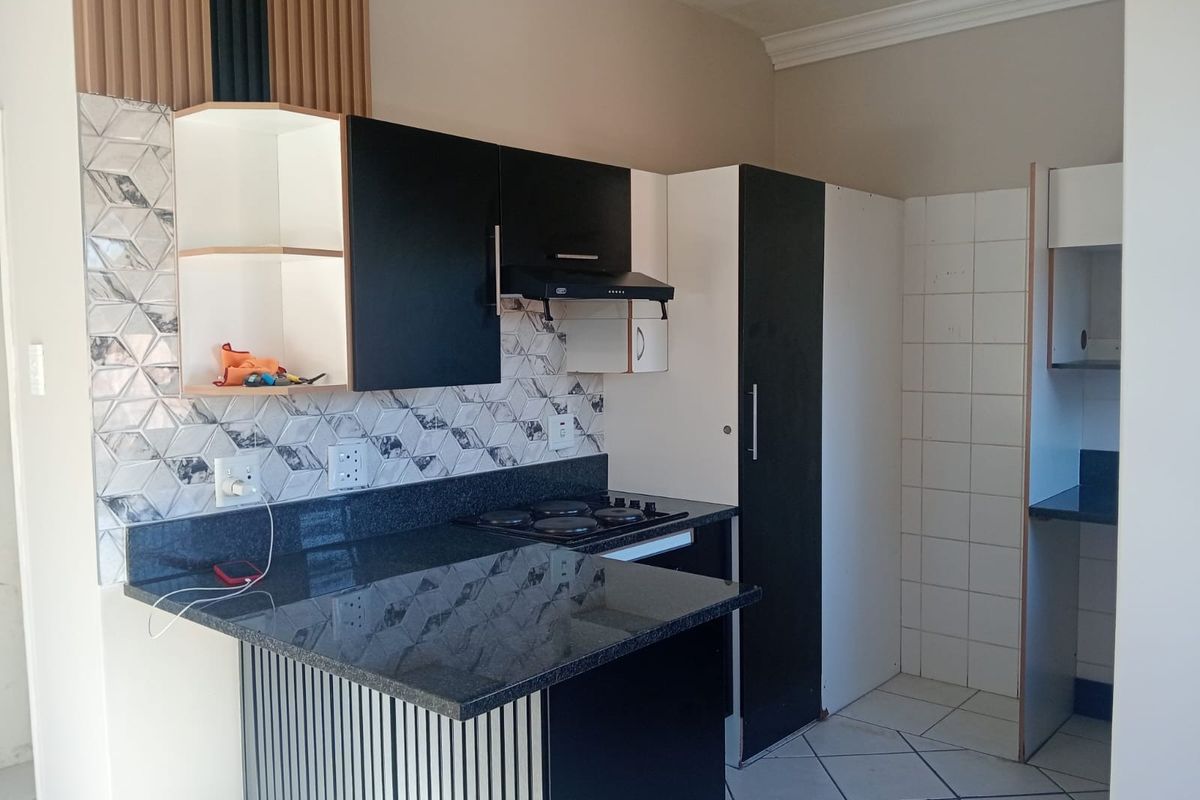 A compact kitchen featuring modern black and white cabinetry, granite countertops, a built-in hob with extractor fan, and decorative geometric tiled backsplash.