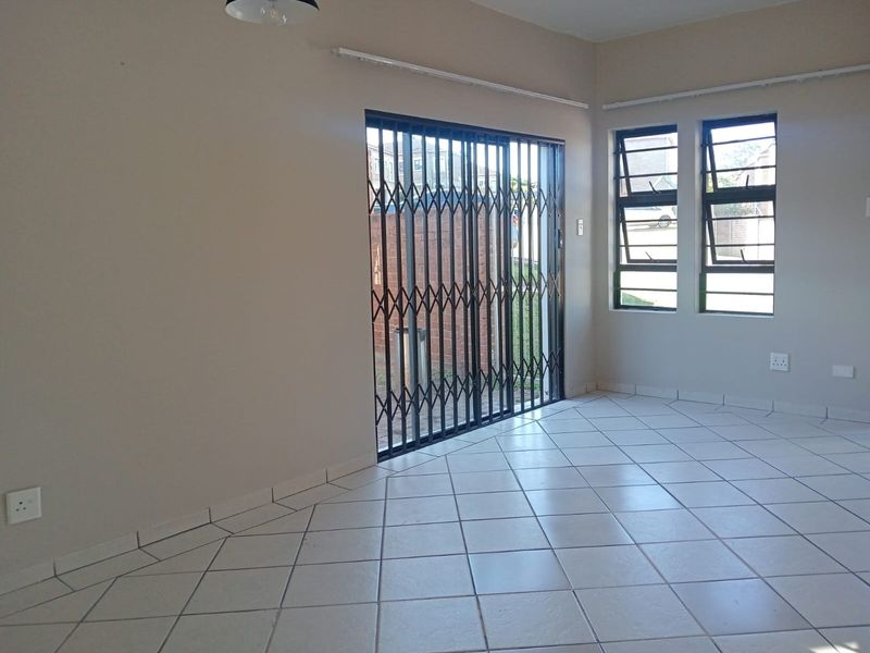 An empty living area featuring neutral tiled flooring, large windows for natural light, and a secure metal sliding gate leading to the exterior.