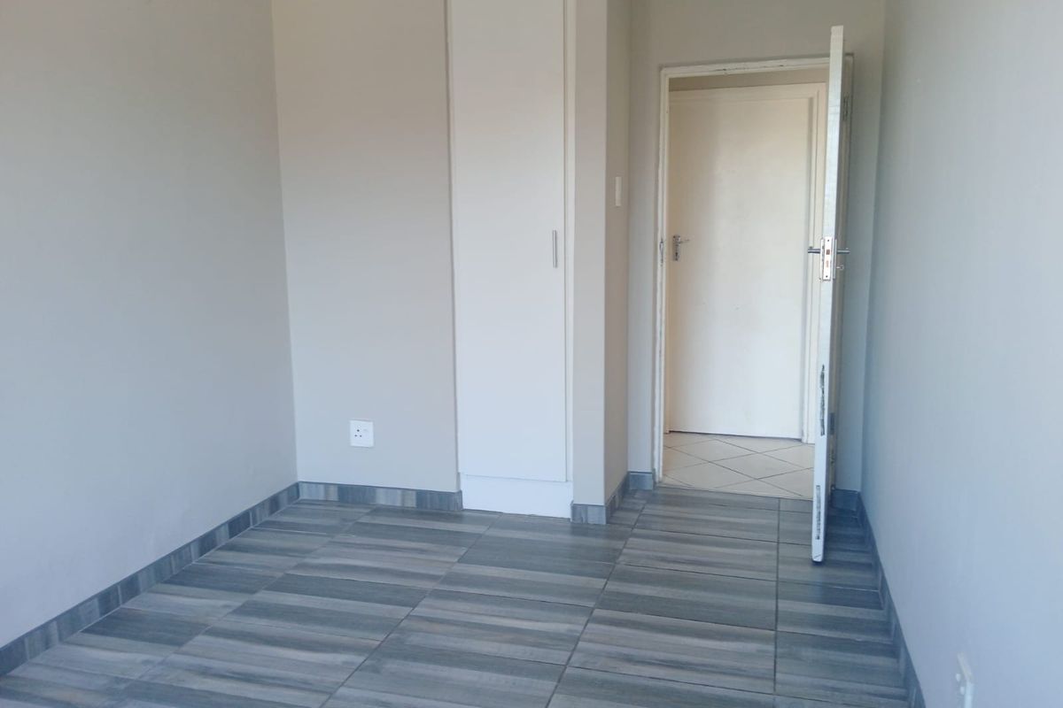 An empty bedroom featuring modern grey-toned tiled flooring and a built-in cupboard, offering a clean and neutral space ready for personalization.