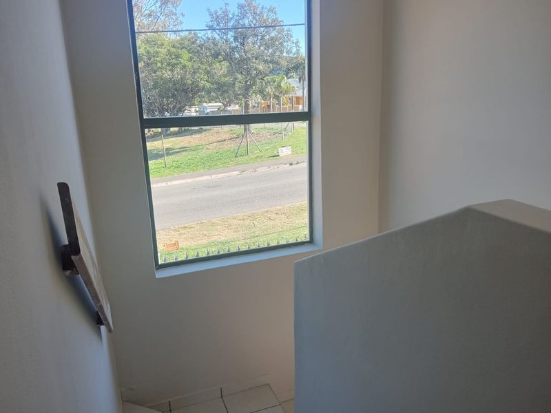 A simple staircase landing area featuring tiled flooring, a wall-mounted handrail, and a large window providing natural light and street views.