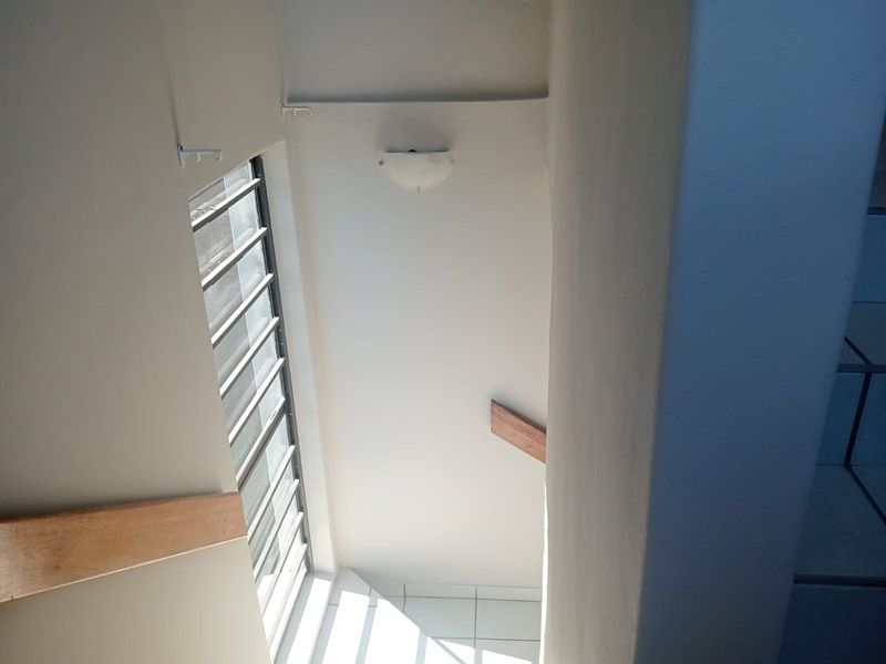 A view looking down a stairwell featuring tiled flooring, a louvered window, and a wooden handrail.