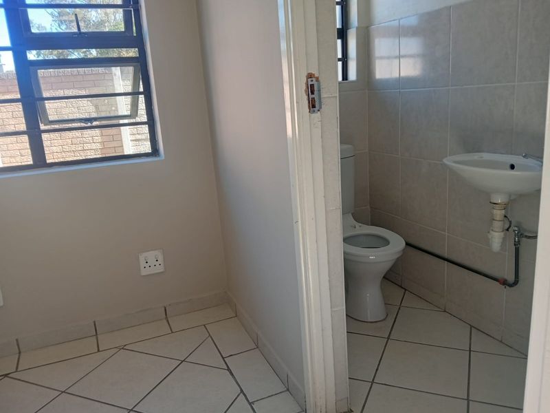 A functional bathroom featuring ceramic floor and wall tiles, a standard toilet, and a pedestal basin with exposed plumbing.