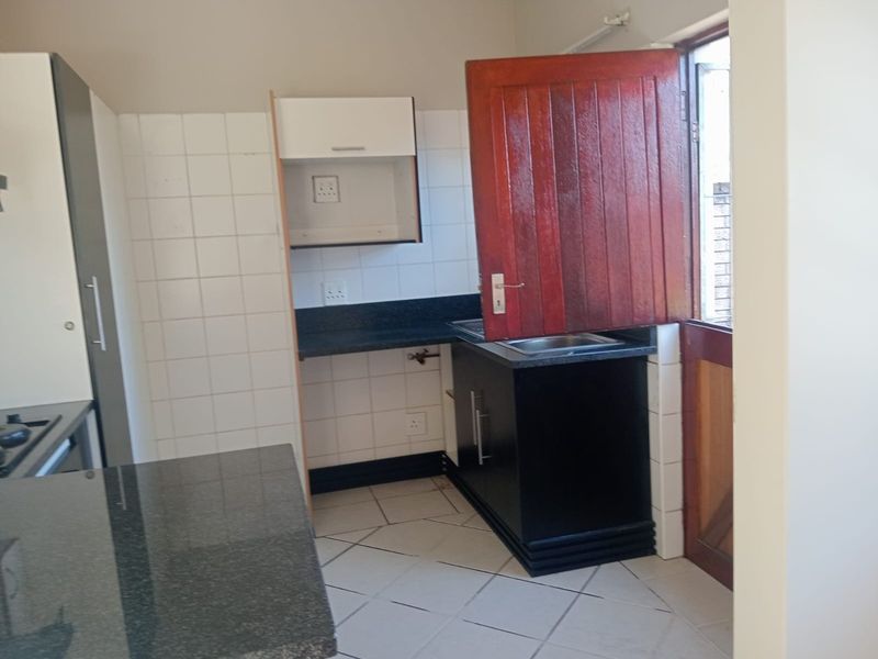 A functional kitchen area featuring granite countertops, built-in cabinetry, a stainless steel sink, and a classic stable door leading to the exterior.