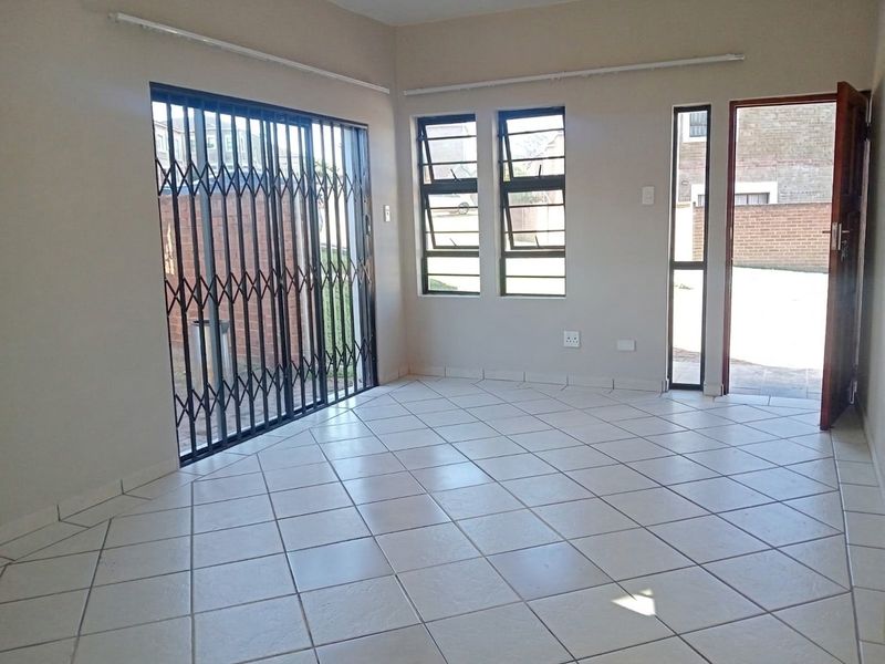 An empty living area featuring neutral tiled flooring, security gates, and direct access to the exterior through a door and sliding gate.