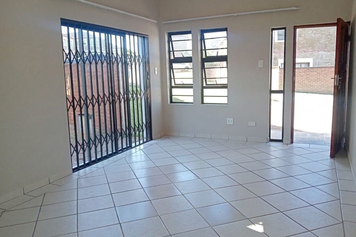 An empty living area featuring neutral tiled flooring, security gates, and direct access to the exterior through a door and sliding gate.