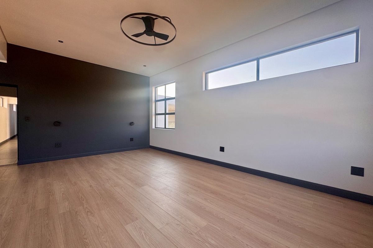 A bright, modern bedroom featuring light wood-look flooring, a dark accent wall, and a contemporary ceiling fan.