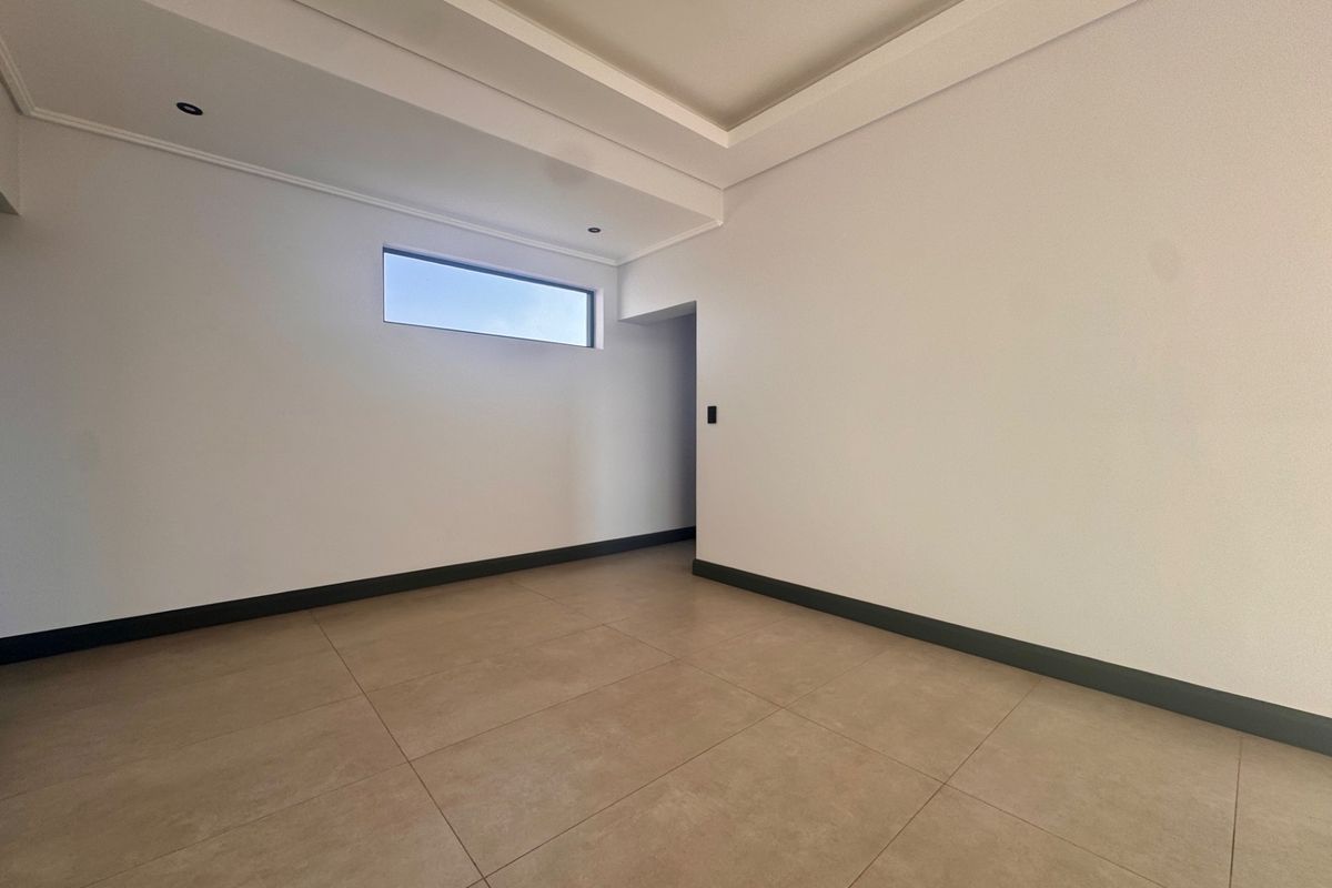 A bright, empty room featuring neutral floor tiles, recessed ceiling detail, and a high-set horizontal window.