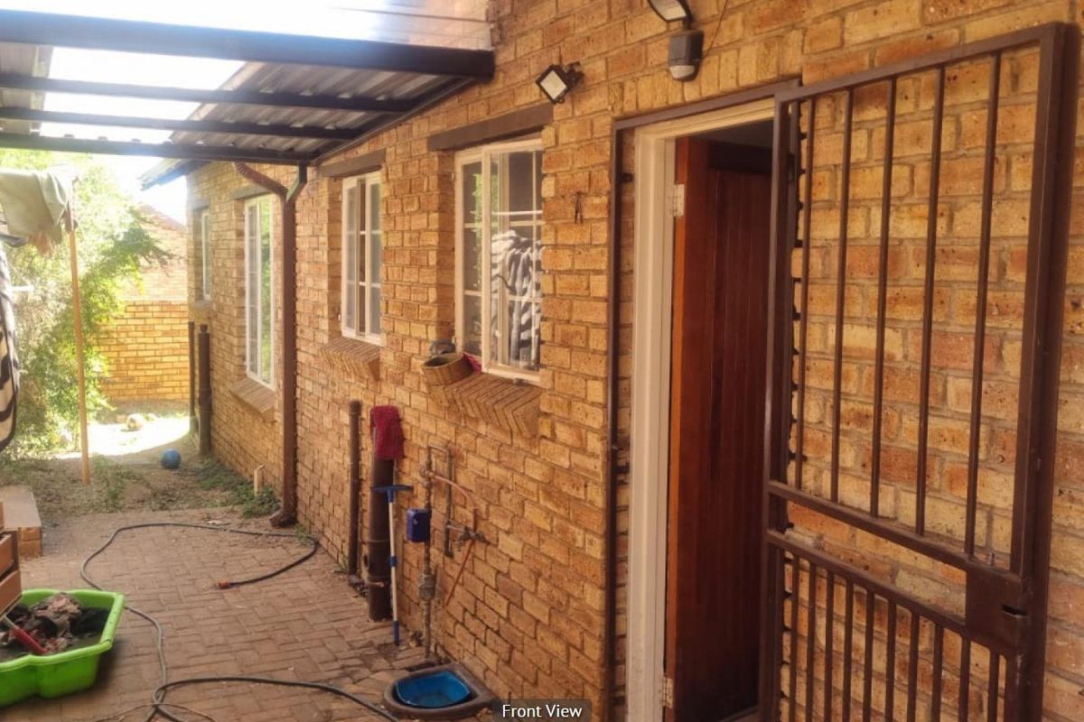 Exterior view of the townhouse side entrance featuring face-brick walls, a covered patio area, and a security gate.