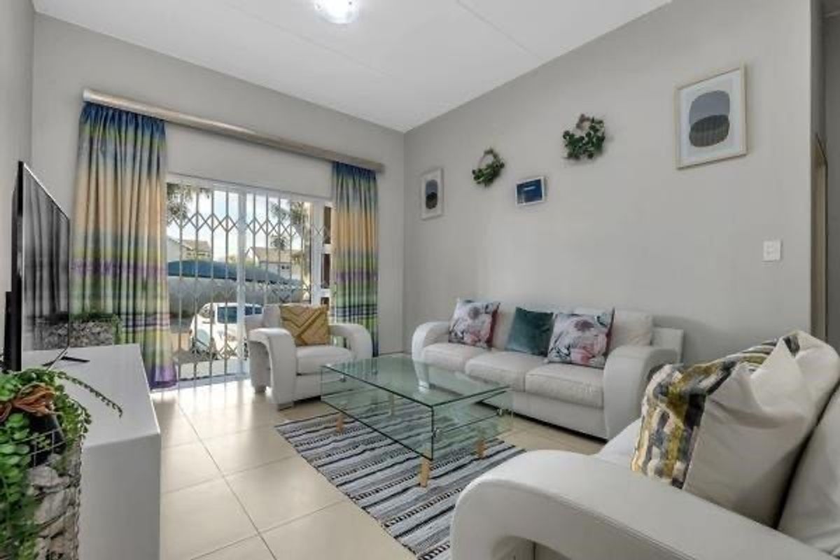A bright living room featuring tiled flooring, large sliding glass doors with security gates, and neutral wall finishes.