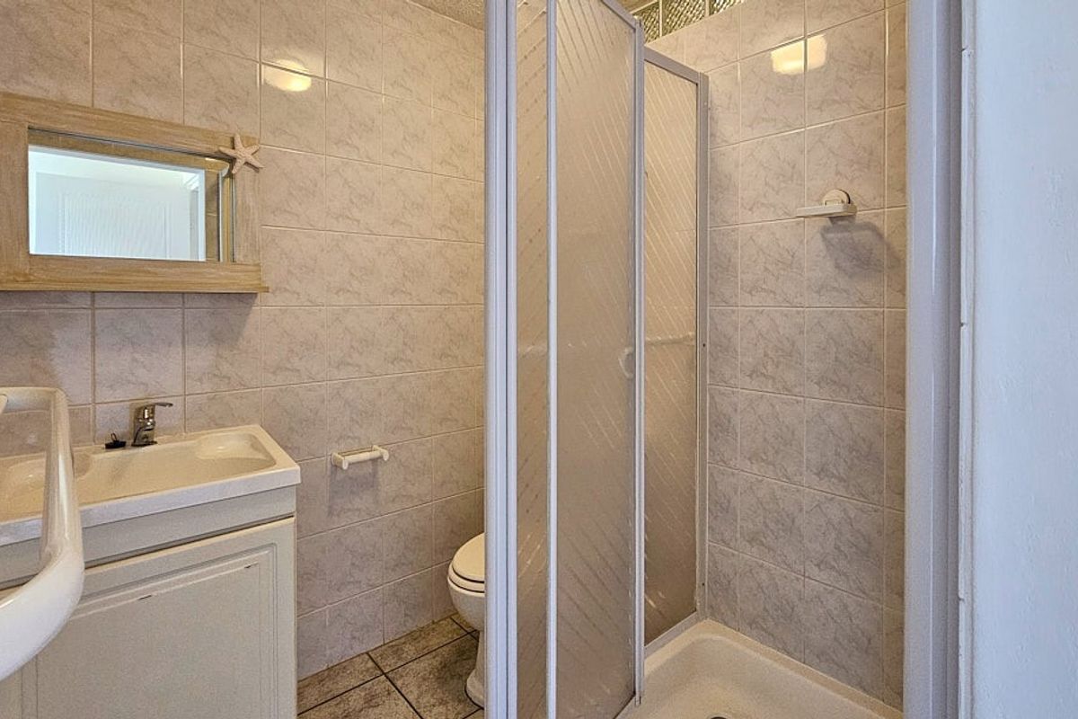 A functional bathroom featuring a shower cubicle with sliding doors, a vanity basin with storage, and full-height wall tiling.
