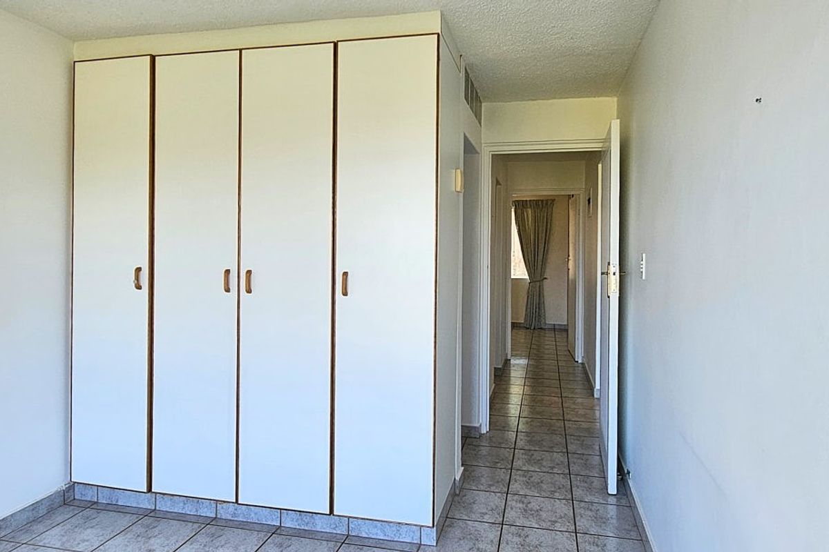 A bedroom featuring built-in white cabinetry and tiled flooring, leading into a hallway with access to other areas of the apartment.
