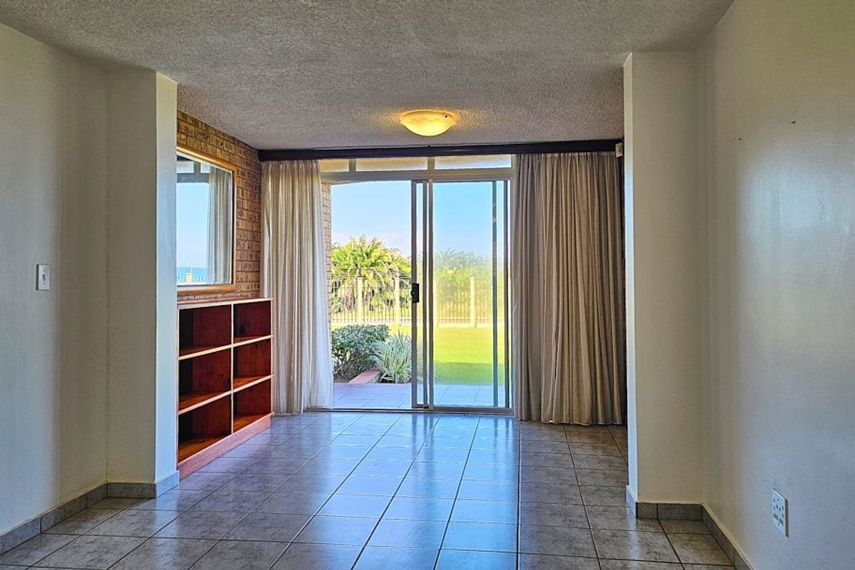 A bright living area featuring tiled flooring, a built-in wooden shelving unit, and large sliding glass doors opening onto a private garden patio.