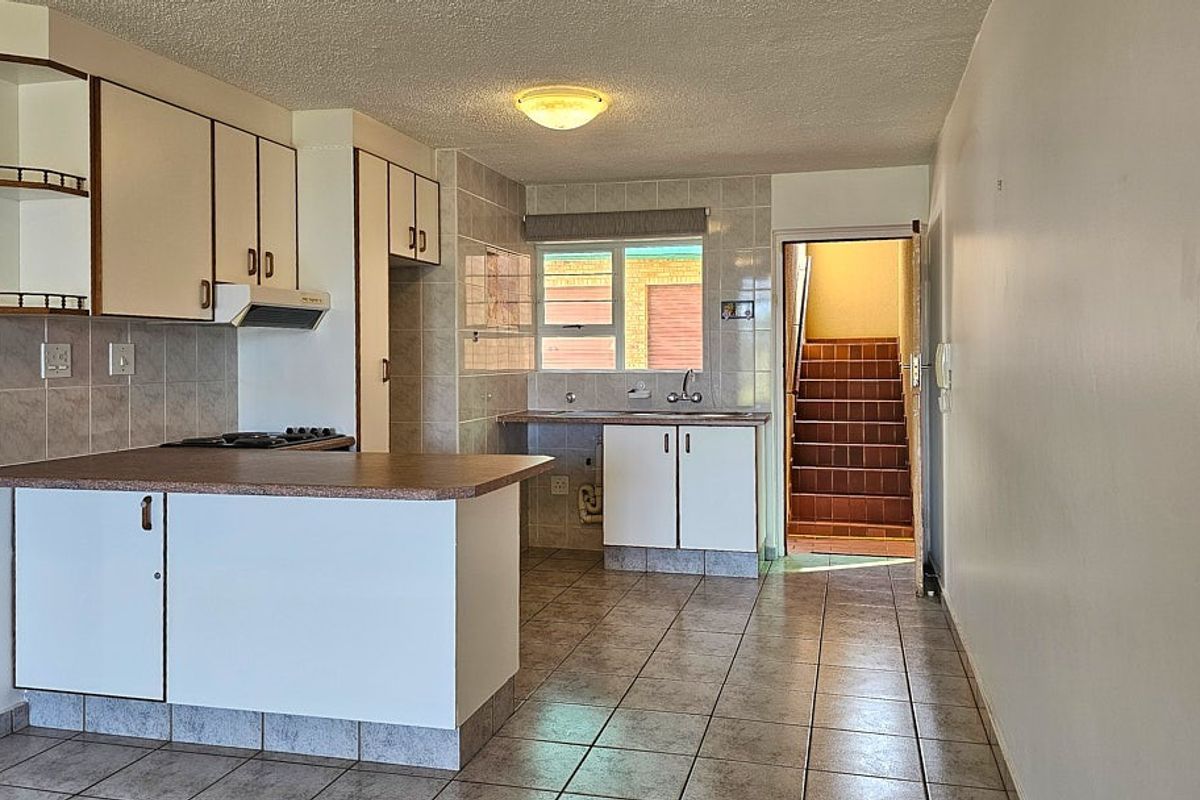 Functional kitchen featuring tiled flooring, built-in cabinetry, a stove hob, and an extractor fan, with direct access to an internal stairwell.