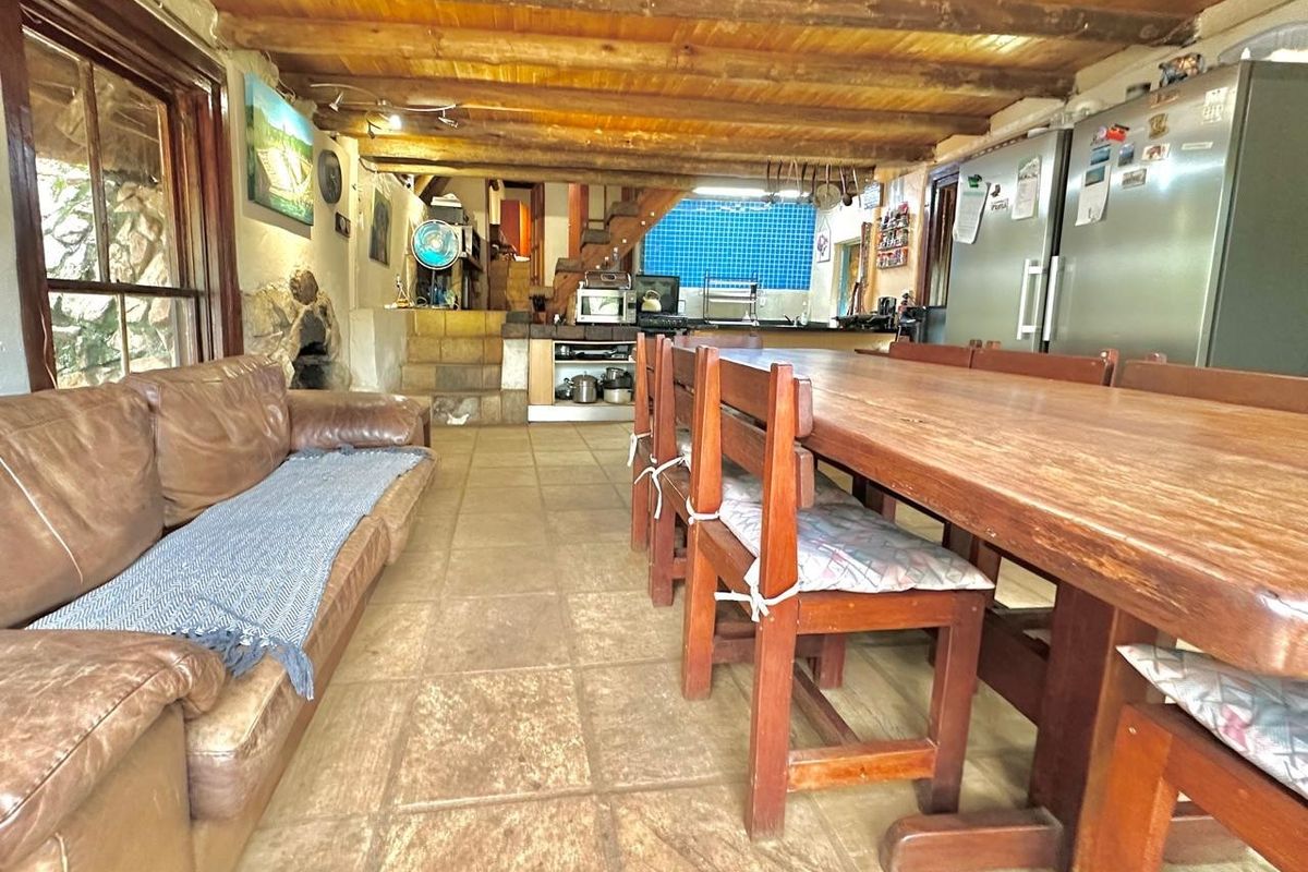 Spacious open-plan living and dining area featuring rustic exposed timber beams, stone wall accents, and a functional kitchen with blue tiled backsplash.