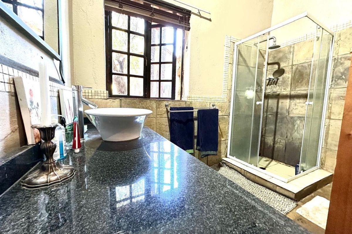Bathroom featuring a granite vanity with a vessel sink, a glass-enclosed shower, and timber-framed windows with natural light.