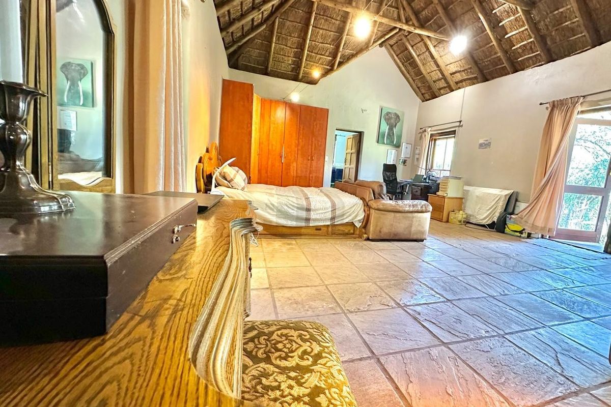 Spacious bedroom featuring a high vaulted thatched ceiling with exposed timber trusses, stone tile flooring, and built-in storage cupboards.