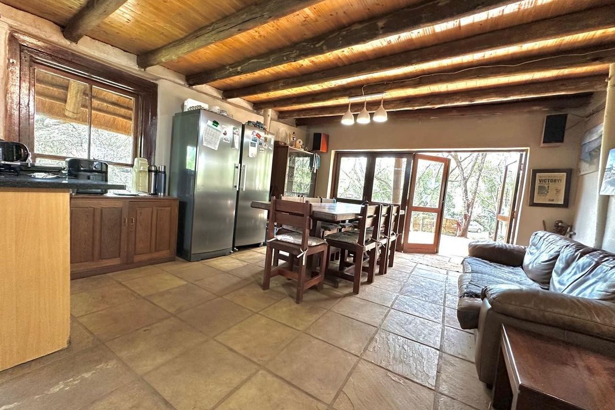 Open-plan living and dining area featuring rustic exposed timber beam ceilings, stone tile flooring, and direct access to the outdoor space through timber doors.