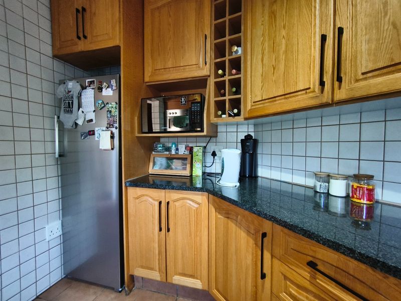 A kitchen featuring traditional oak cabinetry, dark granite countertops, and tiled splashbacks with a built-in microwave shelf and wine rack.