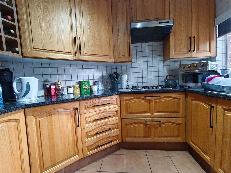 A functional kitchen featuring traditional oak cabinetry, dark granite countertops, a built-in gas hob, and an extractor fan with tiled splashbacks.