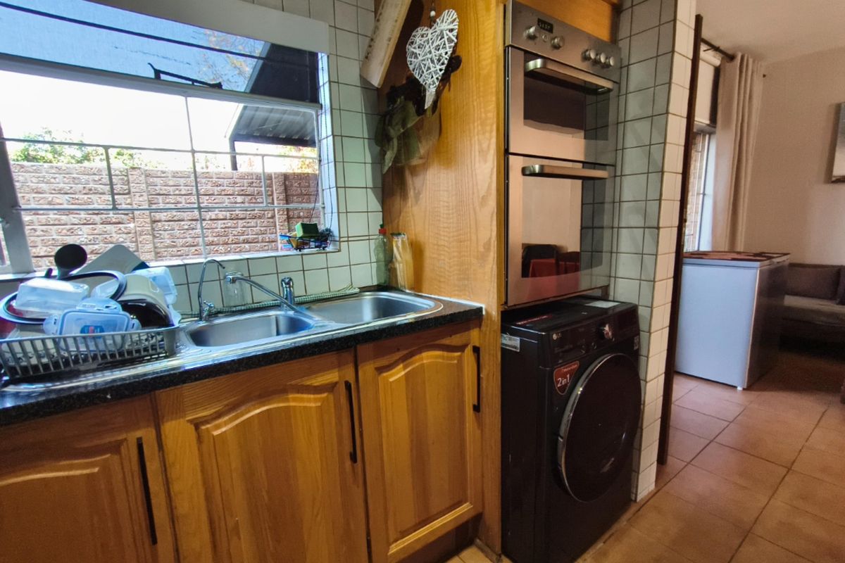 A functional kitchen featuring wooden cabinetry, a double stainless steel sink, built-in double oven, and tiled splashbacks with a view to the rear exterior.