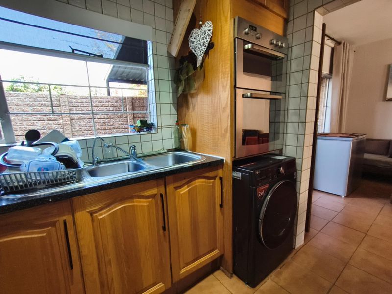 A functional kitchen featuring wooden cabinetry, a double stainless steel sink, built-in double oven, and tiled splashbacks with a view to the rear exterior.